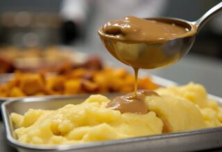 Brown potato gravy being poured onto more potatoes, mashed. Concept for bland, tasteless, unappetizing food, everyday canteen, prison food serving, soup kitchen, feeding the homeless, poor, refugees. By Sweeann - AdobeStock. Généré à l'aide de l'IA