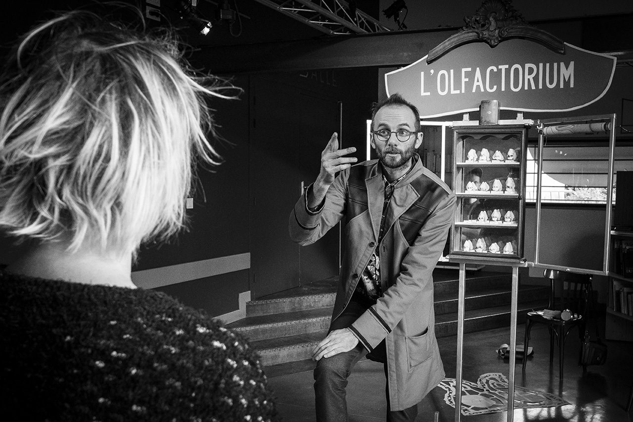 À l’accueil du public, un premier intervenant explique les connaissances acquises sur le monde des odeurs. Derrière lui, différents moulages de nez sont posés sur les étagères d’un olfactorium. © Philippe Lamotte