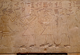 bas relief égyptien, 4 personnages sont représenté en pied, celle de gauche fait face aux trois autres. La pierre semble être un linteau. Des inscriptions en hiéroglyphe sont gravé au dessus des personnages